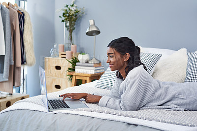 Buy stock photo Shot of an attractive young woman using a laptop while chilling on her bed in her bedroom at home