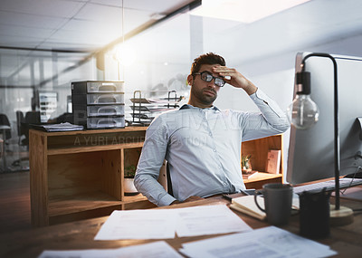 Buy stock photo Shot of a young businessman looking stressed out while working late on a computer in an office