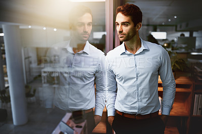 Buy stock photo Shot of a young businessman standing in an office at night