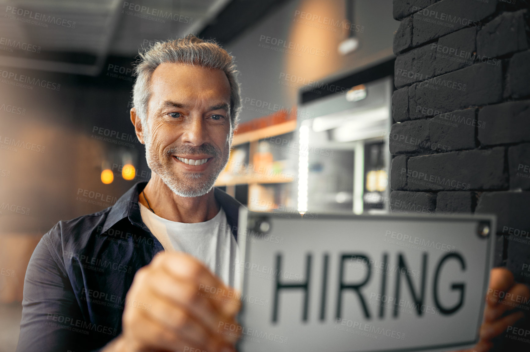 Buy stock photo Cropped portrait of a handsome mature man holding up a hiring sign while standing in his coffee shop