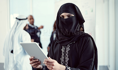Buy stock photo Cropped portrait of an attractive young arabic businesswoman working on a tablet in the office with her colleagues in the background