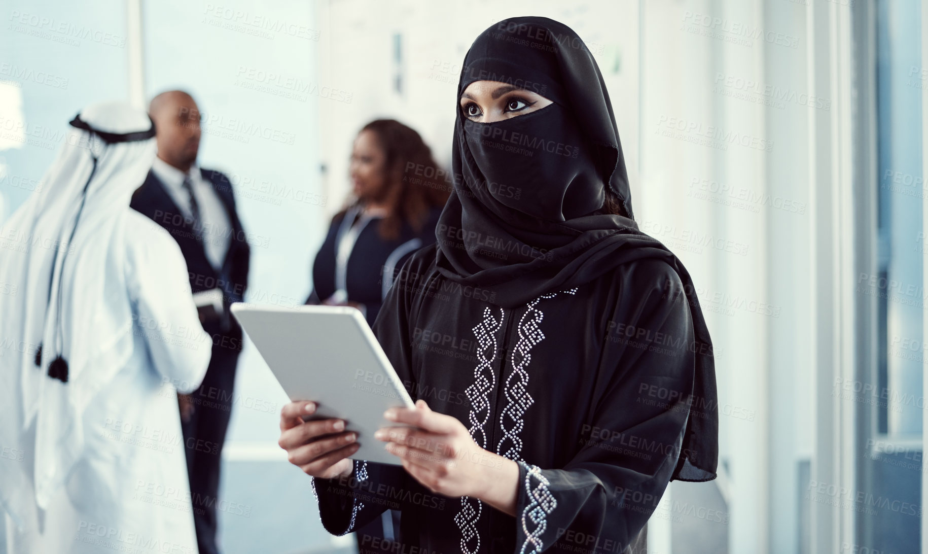 Buy stock photo Cropped shot of an attractive young arabic businesswoman working on a tablet in the office with her colleagues in the background