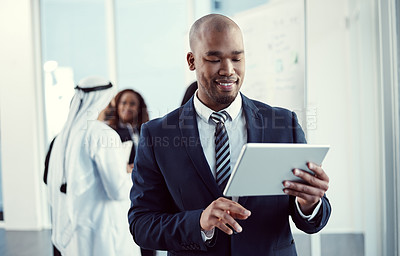 Buy stock photo Cropped shot of a handsome young businessman working on a tablet in the office with his colleagues in the background