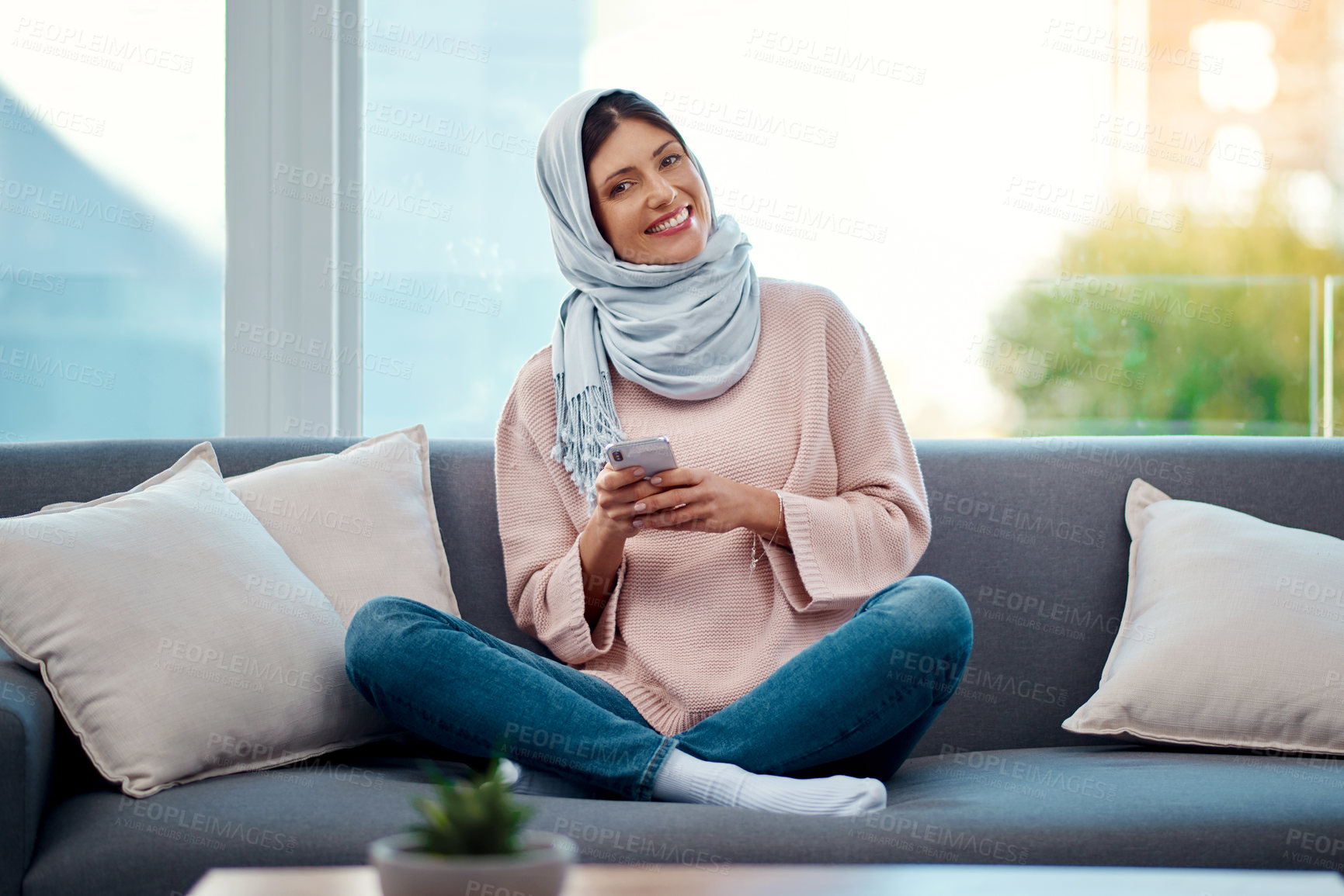 Buy stock photo Smile, phone and portrait of muslim woman on sofa typing email on mobile app or internet at home. happy, technology and islamic female person scroll on cellphone and relaxing in living room at house.
