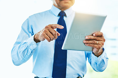 Buy stock photo Shot of an unrecognizable man browsing on a digital tablet inside of a building during the day
