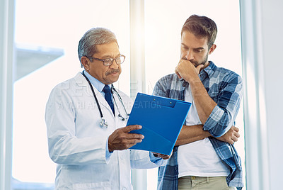 Buy stock photo Shot of a confident mature male doctor showing test results to a patient inside of a hospital during the day