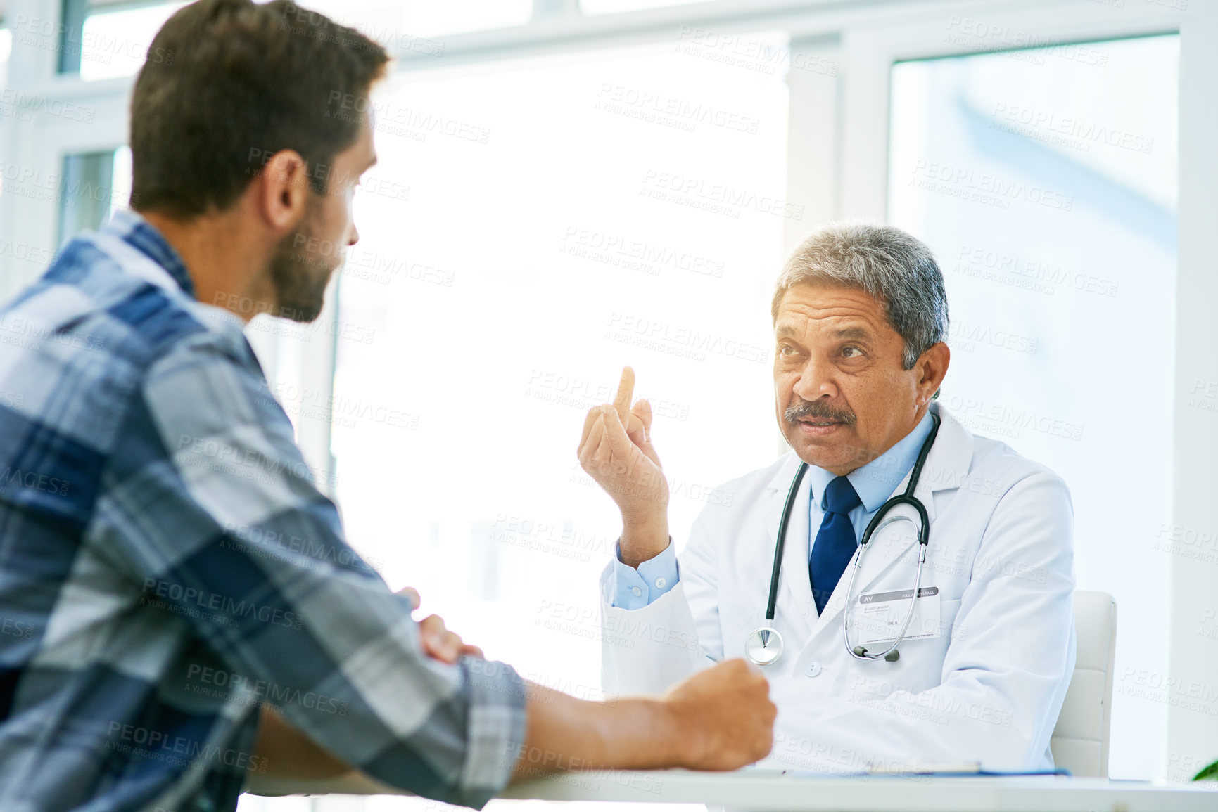 Buy stock photo Shot of a confident mature male doctor consulting with a patient inside of his office during the day