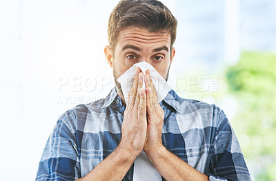 Buy stock photo Portrait of an uncomfortable looking young man blowing his nose with a tissue inside of a building during the day