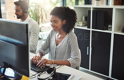 Buy stock photo Shot of a young businesswoman working on her computer with her colleague in the background