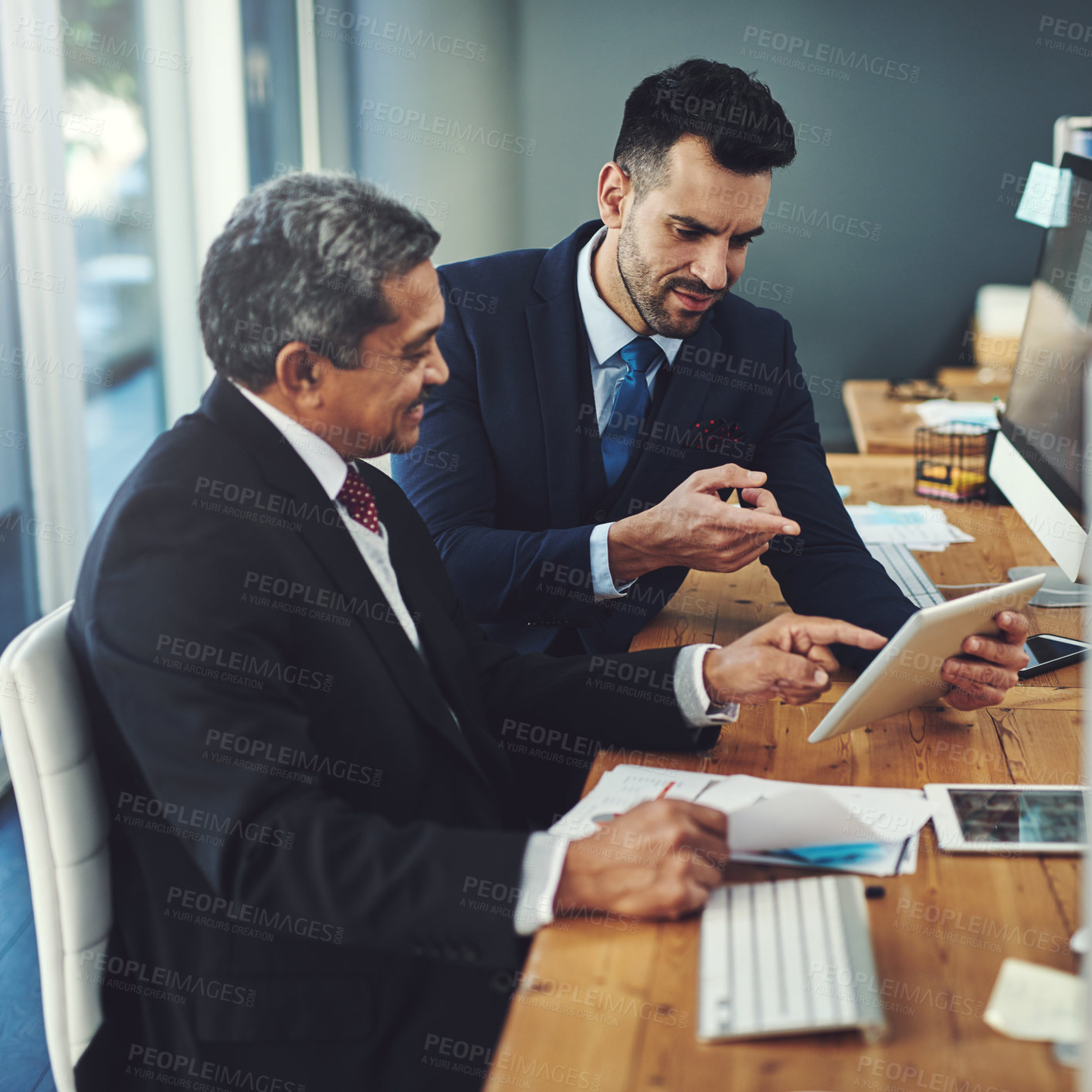 Buy stock photo Shot of two businessmen working on a digital tablet in an office