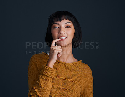 Buy stock photo Studio portrait of an attractive young woman biting her finger against a dark background
