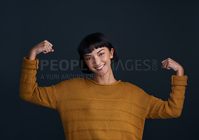 Buy stock photo Studio shot of an attractive young woman flexing her muscles against a dark background