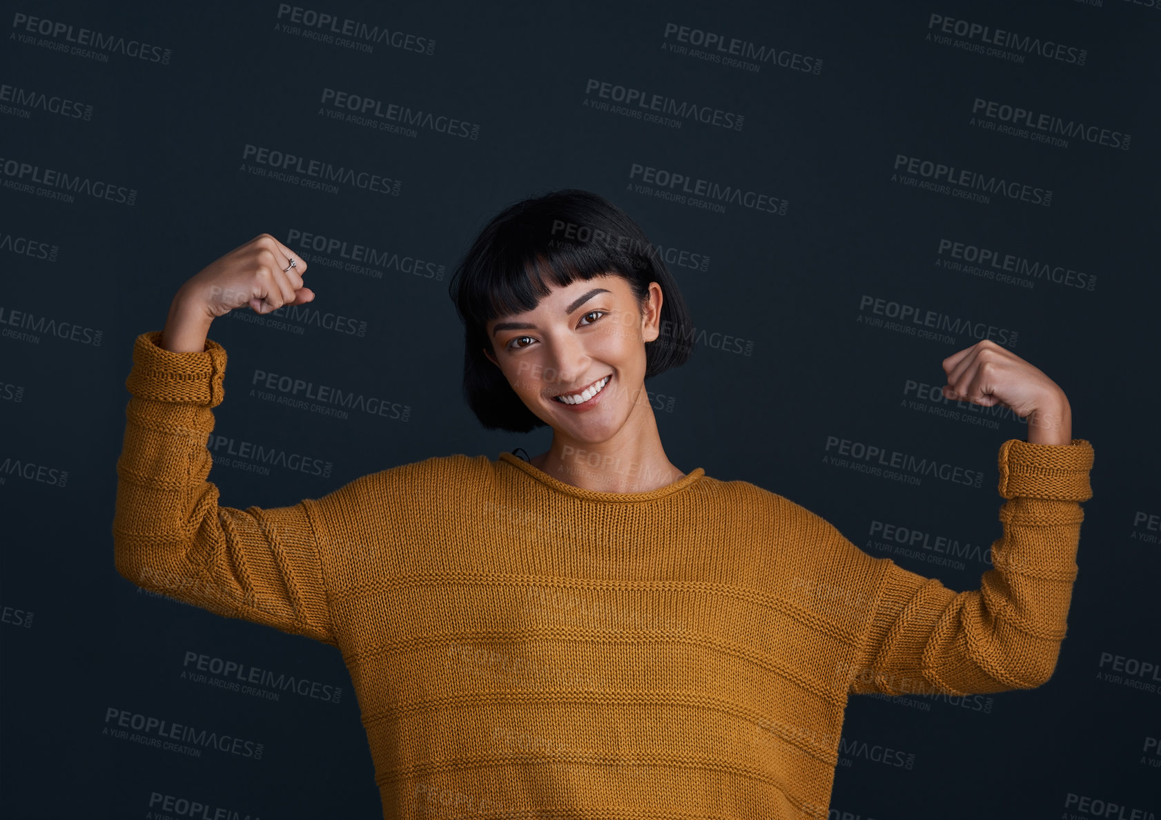 Buy stock photo Studio shot of an attractive young woman flexing her muscles against a dark background