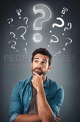 Buy stock photo Studio shot of a handsome young man looking thoughtful while standing underneath an illustration of question marks against a grey background