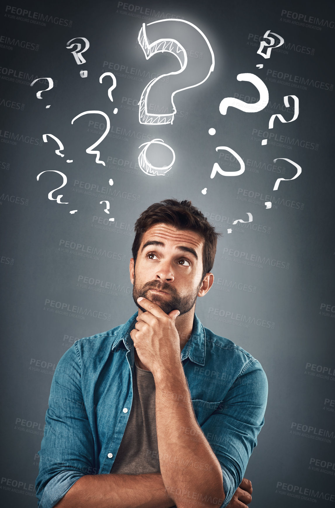 Buy stock photo Studio shot of a handsome young man looking thoughtful while standing underneath an illustration of question marks against a grey background