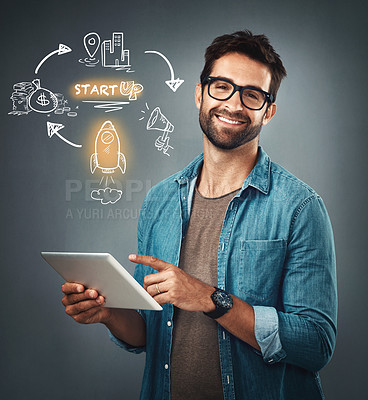 Buy stock photo Studio portrait of a handsome young man browsing on a digital tablet while standing next to illustrations against a grey background