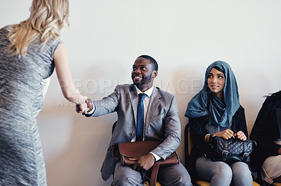Buy stock photo Shot of a cheerful young business receiving a handshake from a businesswoman while waiting for a interview inside of a office during the day