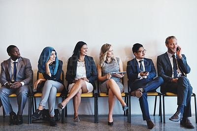 Buy stock photo Shot of a group of confident businesspeople waiting in line for their interviews while a man talks loudly on his cellphone inside of a office during the day