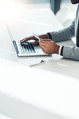 Buy stock photo High angle shot of an unrecognizable businessman holding his credit card while using a laptop at his desk
