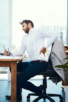 Buy stock photo Shot of a young businessman suffering from back pain while working in an office