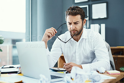 Buy stock photo Shot of a young businessman looking serious while working on a laptop in an office