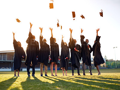 Buy stock photo Shot of a group of university students throwing their hats in the air on graduation day