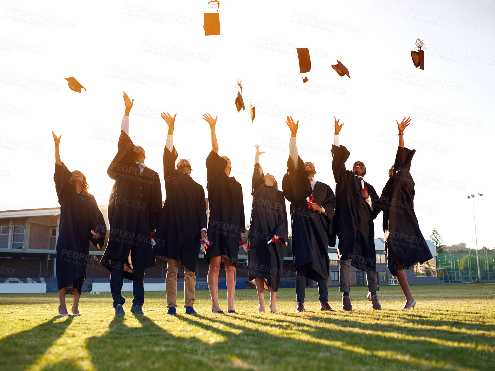 Buy stock photo Shot of a group of university students throwing their hats in the air on graduation day