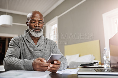 Buy stock photo Shot of a senior man using a mobile while working on his finances at home
