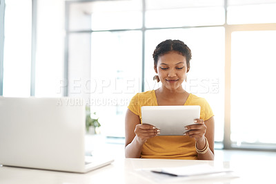 Buy stock photo Shot of a young businesswoman using a laptop and digital tablet at her desk in a modern office