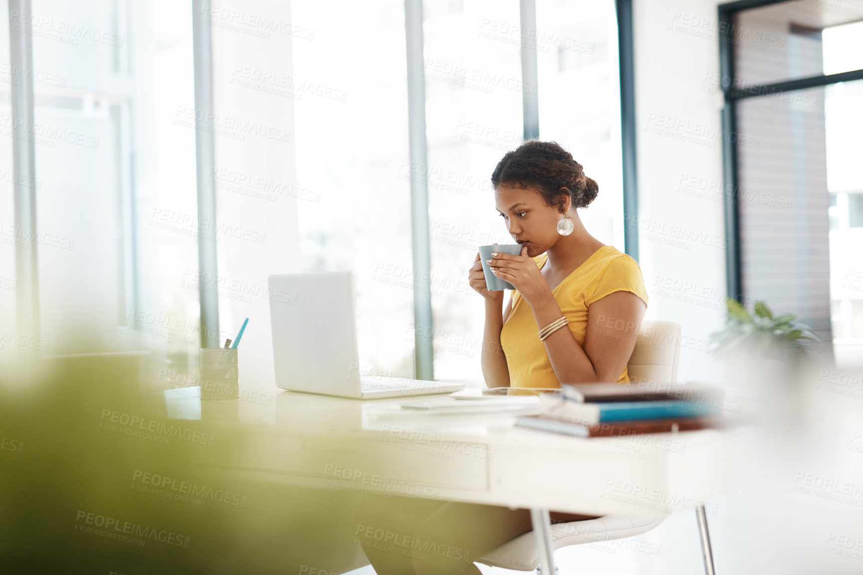 Buy stock photo Shot of a young businesswoman using a laptop and drinking a beverage at her desk in a modern office