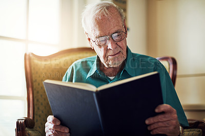 Buy stock photo Cropped shot of a senior man reading a book while relaxing at home