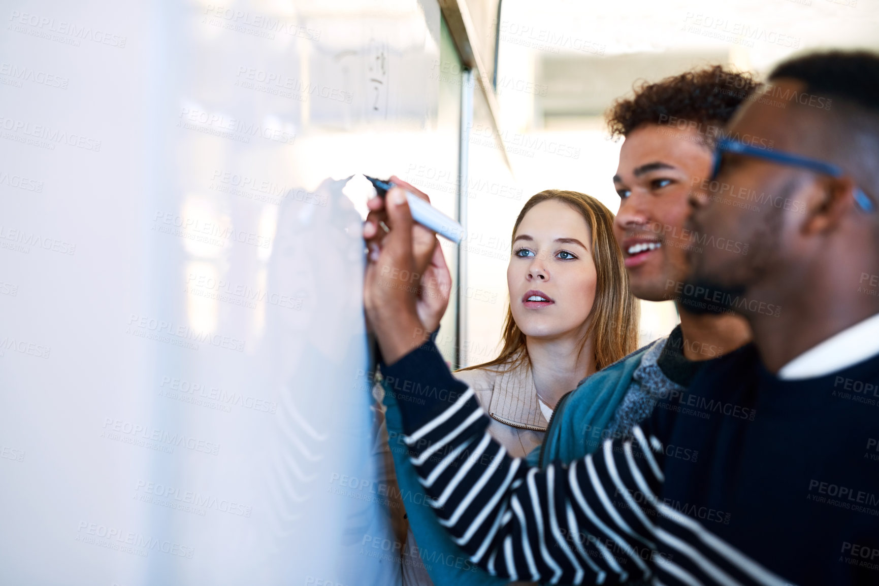 Buy stock photo Shot of a young man writing on a whiteboard while students look on