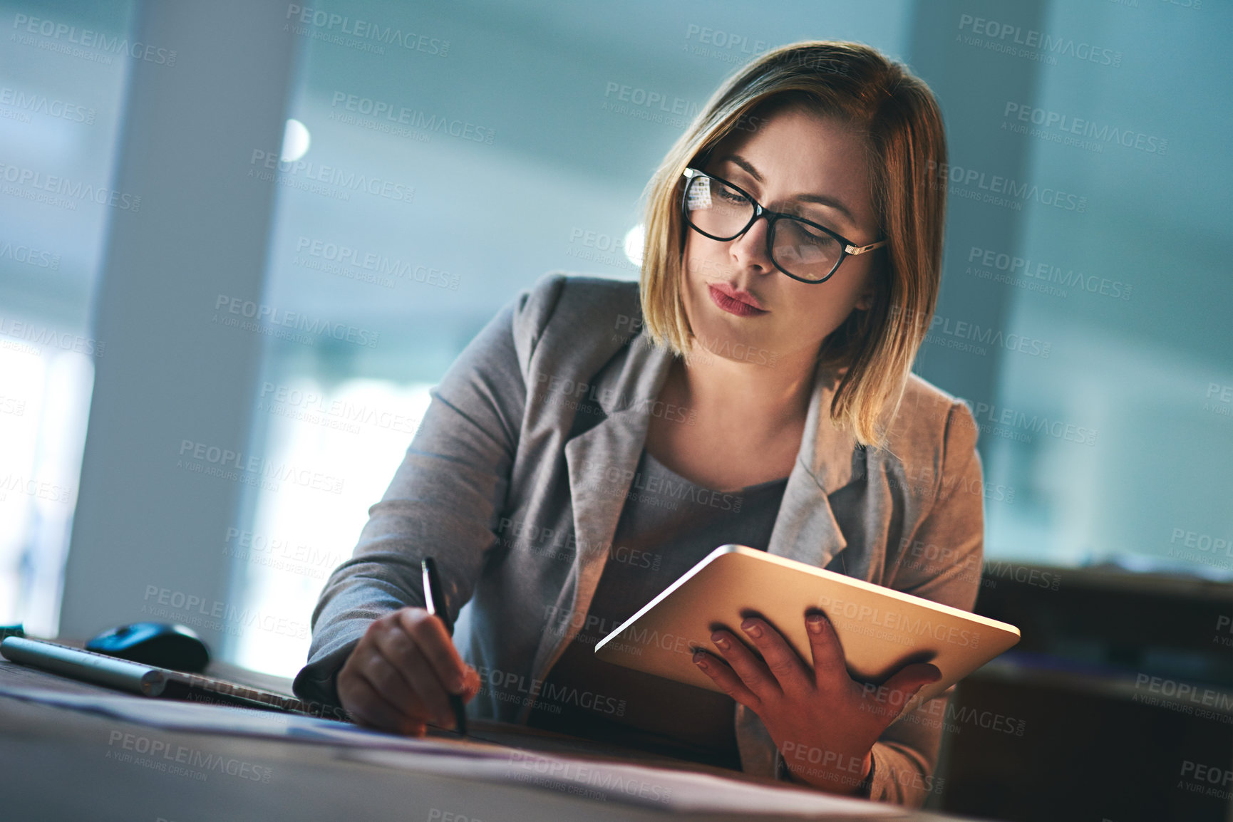 Buy stock photo Shot of a young businesswoman working late on a digital tablet in an office