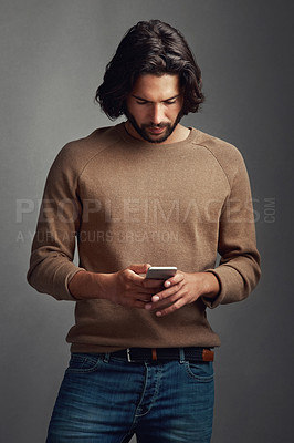 Buy stock photo Studio shot of a handsome young man using a mobile phone against a gray background