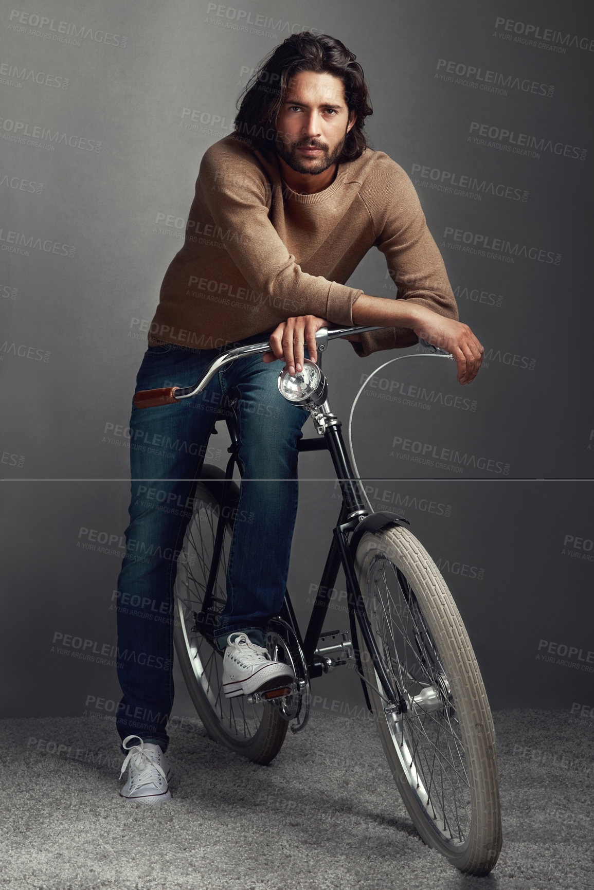 Buy stock photo Studio shot of a handsome young man leaning against a bicycle in front of a gray background
