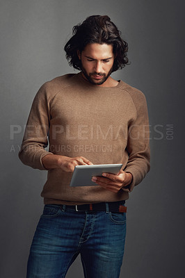 Buy stock photo Studio shot of a handsome young man using a digital tablet against a gray background