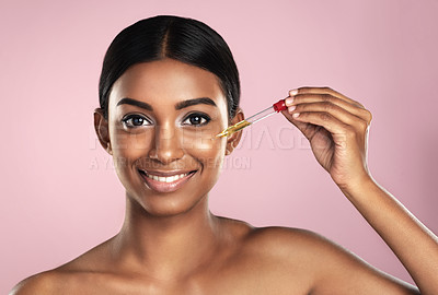 Buy stock photo Face, skincare serum and happy woman in studio isolated on a pink background. Portrait, cosmetics and Indian model with hyaluronic acid, essential oil or vitamin c dropper for healthy dermatology.