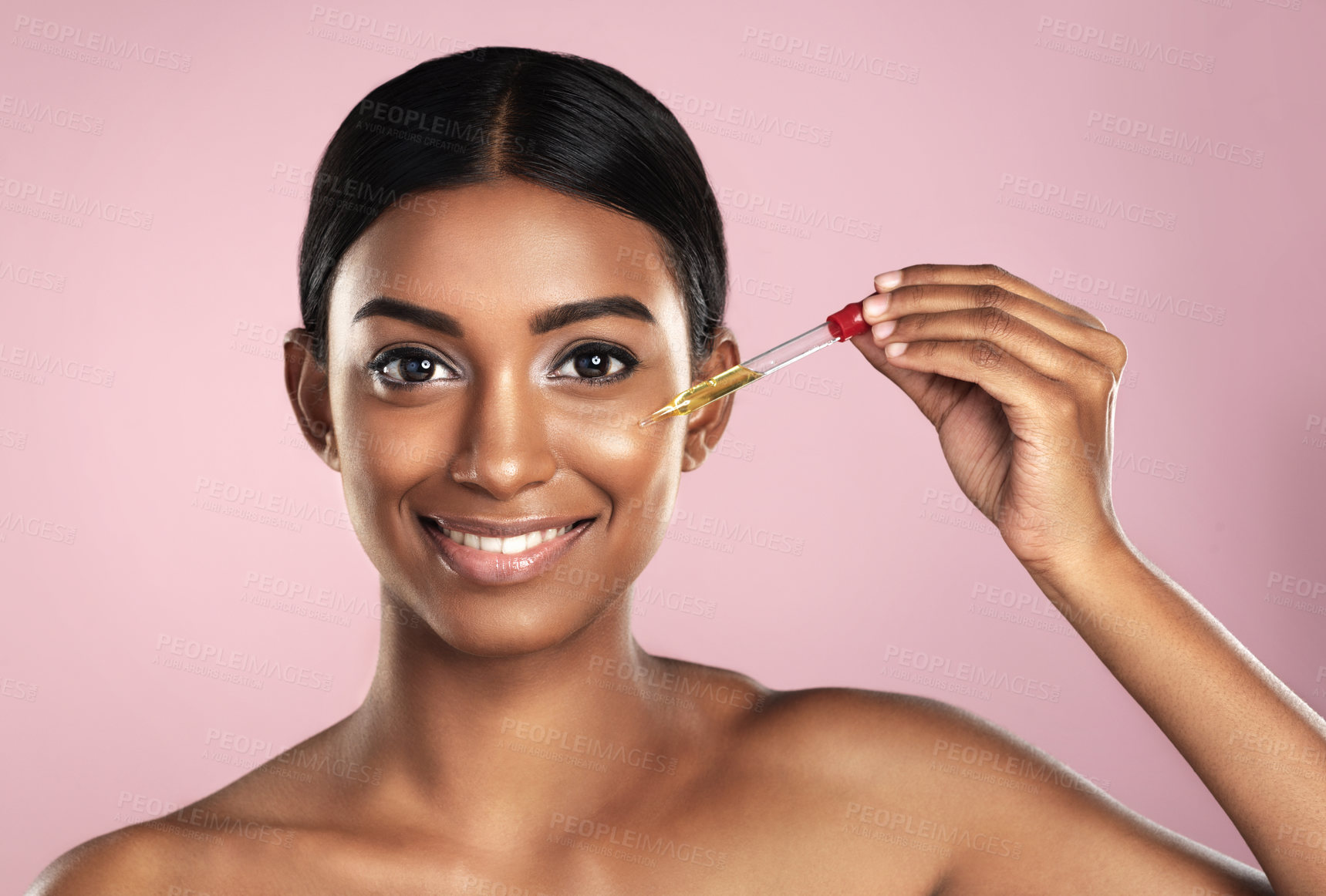 Buy stock photo Face, skincare serum and happy woman in studio isolated on a pink background. Portrait, cosmetics and Indian model with hyaluronic acid, essential oil or vitamin c dropper for healthy dermatology.