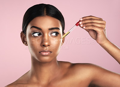Buy stock photo Face, skincare serum and serious woman in studio isolated on a pink background. Dermatology, cosmetics and Indian model with hyaluronic acid, essential oil or apply vitamin c dropper for healthy skin