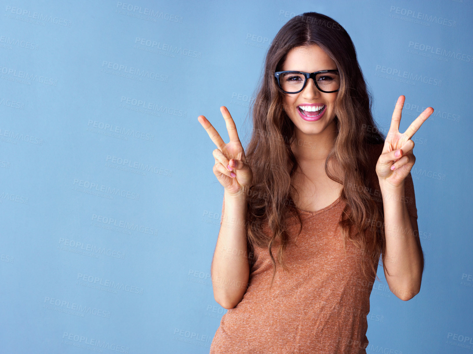 Buy stock photo Portrait, hands and happy woman with peace sign in studio for excitement, good mood or expression on blue background. V, emoji and model with glasses for gesture, positive attitude or smile mockup