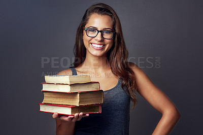 Buy stock photo Studio portrait of a young woman holding a pile of books against a grey background