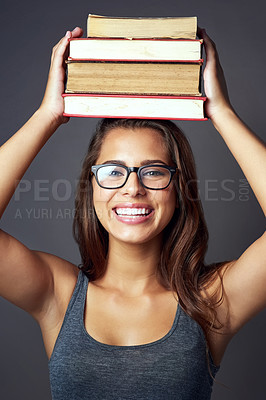 Buy stock photo Studio portrait of a young woman balancing a pile of books on her head against a grey background