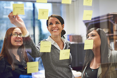 Buy stock photo Cropped shot of a group of businesswomen brainstorming on a glass wall in an office