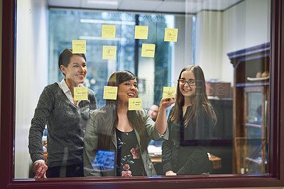 Buy stock photo Cropped shot of a group of businesswomen brainstorming on a glass wall in an office