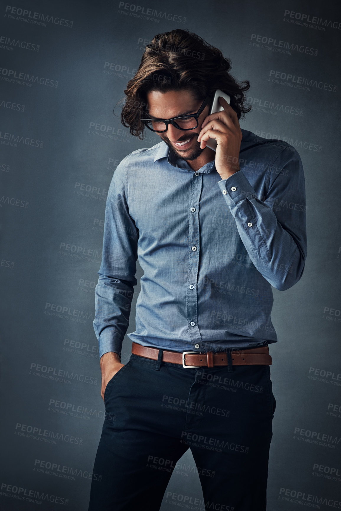 Buy stock photo Studio shot of a handsome young man talking on his cellphone while standing against a grey background