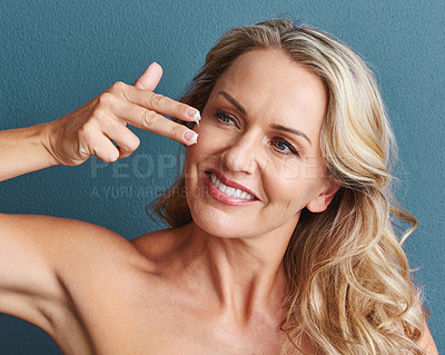 Buy stock photo Studio shot of an attractive mature woman applying moisturizer against a grey background