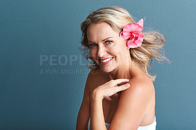 Buy stock photo Studio portrait of an attractive mature woman posing with a flower in her hair against a grey background