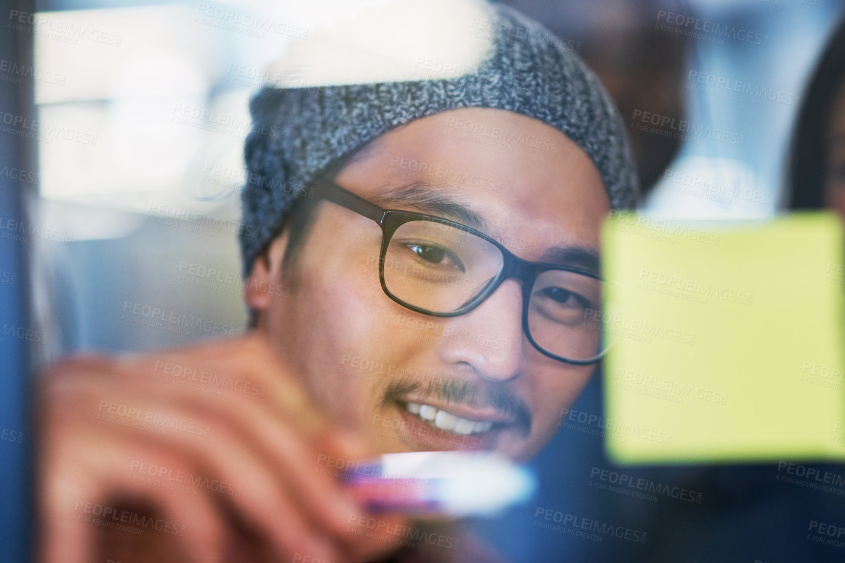 Buy stock photo Shot of a young businessman brainstorming with notes on a glass wall in an office