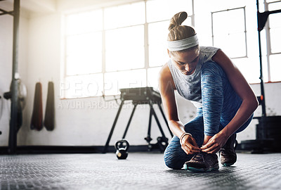 Buy stock photo Shot of an attractive young woman tying her shoelaces at the gym