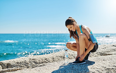 Buy stock photo Shot of a sporty young woman tying her shoelaces while out for a run